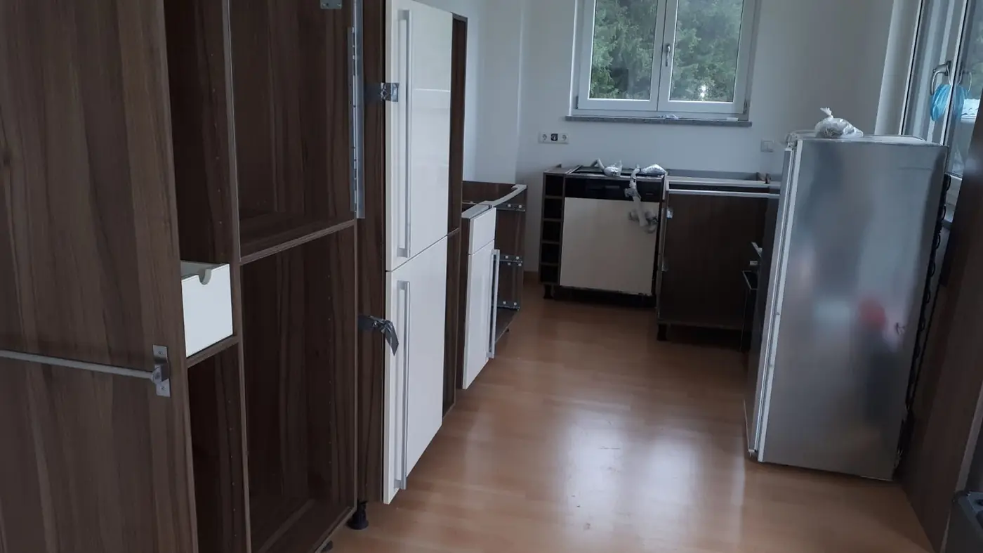 Küche während der Montage in München: aufgestellte Korpusse, teilweise montierte weiße Fronten und noch nicht eingebauter Geschirrspüler